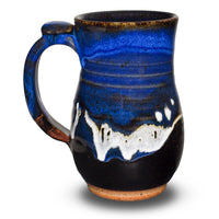 20 oz. wheel-thrown mug in Blue-Black color combination. It's handmade pottery by Prairie Fire Pottery, accented by a meandering ribbon of white that breaks into a delicate gold at the edges. At the top of the handle is a thumb-rest giving this mug better balance and a nicer grip. On the bottom it is signed and dated with Tama's inscribed signature. Like everything at Prairie Fire Pottery it is handmade in stoneware clay, lead-free, microwavable, and food and dishwasher-safe.