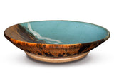 A large turquoise-brown bowl with ribbons of white and a swath of red over toasted brown.  Sideview.