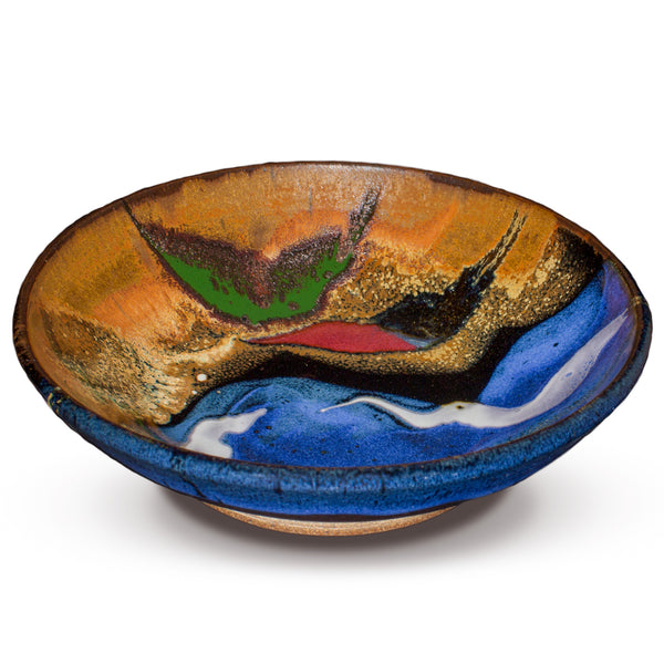 A 7-inch medium bowl with a blend of toasted orange, cobalt blue, red, crystal yellow, and white colors, wheel-thrown in stoneware clay and high-fired.  Handmade pottery by Prairie Fire Pottery.  3/4 view.