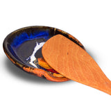 Beautiful handmade pottery spoon rest in cobalt blue and toasted orange colors. It is handmade pottery by Prairie Fire Pottery. Hand made in stoneware clay.  View of a wooden spoon on the spoon rest..