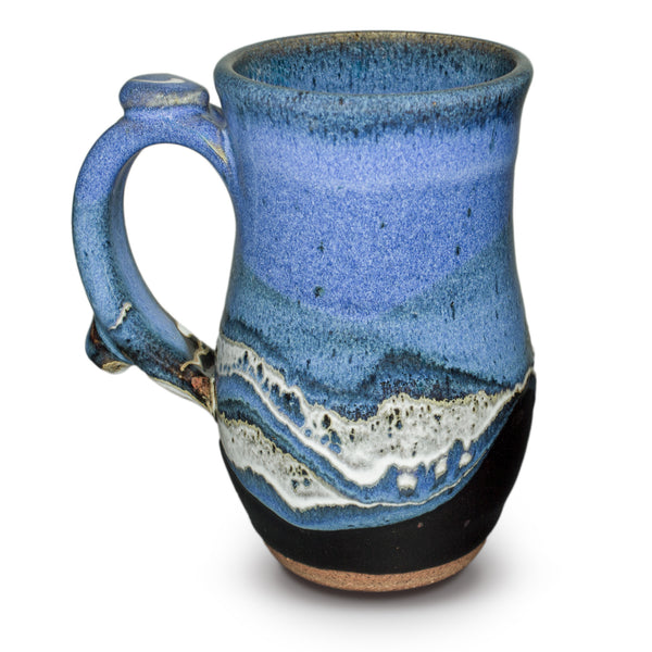 12 oz. wheel-thrown mug in Blue-Black color combination. It's handmade pottery by Prairie Fire Pottery, accented by a meandering ribbon of white that breaks into a delicate gold at the edges. At the top of the handle is a thumb-rest giving this mug better balance and a nicer grip. On the bottom it is signed and dated with Tama's inscribed signature. Like everything at Prairie Fire Pottery it is handmade in stoneware clay, lead-free, microwavable, and food and dishwasher-safe.