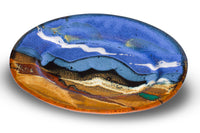 Handmade pottery by Prairie Fire Pottery. 9-inch oval stoneware plate in cobalt blue and toasted orange colors. Accented with red and teal. Hand made in the U.S.A. 3/4 table top view.