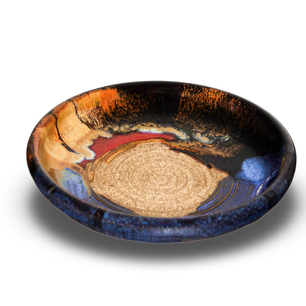 This is a pretty six inch garlic dipping plate in cobalt blue and toasted brown colors . It has a raspy spiral center for breaking up garlic cloves before adding oil and vinegar. Handmade pottery by Prairie Fire Pottery. This is a 3/4 view of the product.