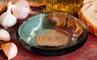 This is a pretty six inch garlic dipping plate in turquoise-brown colors and red. It has a raspy spiral center for breaking up garlic cloves before adding oil and vinegar. Handmade pottery by Prairie Fire Pottery.
