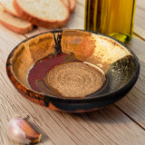 This is a pretty six inch garlic dipping plate in earth tone colors and red. It has a raspy spiral center for breaking up garlic cloves before adding oil and vinegar. Handmade pottery by Prairie Fire Pottery.  This is a tabletop view of the product with french bread.