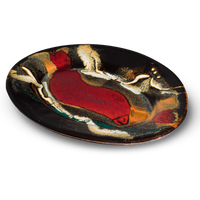 Oval plate with a 9-inch diameter . Handmade pottery by Prairie Fire Pottery. Toasted brown , red, and teal colors against a black background. Table top 3/4 view.