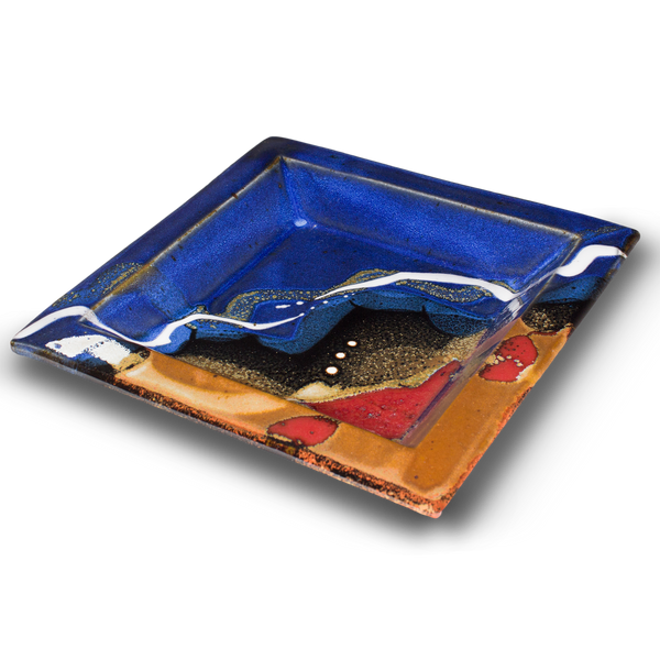 8 inch square plate.  Cobalt blue and toasted brown colors, accented with red.  Handmade pottery from Prairie Fire Pottery.  This is a 3/4 table top view.